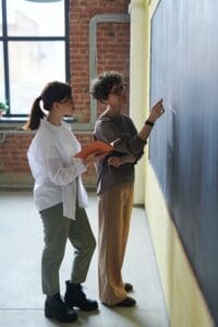 Two people are standing in front of a wall.